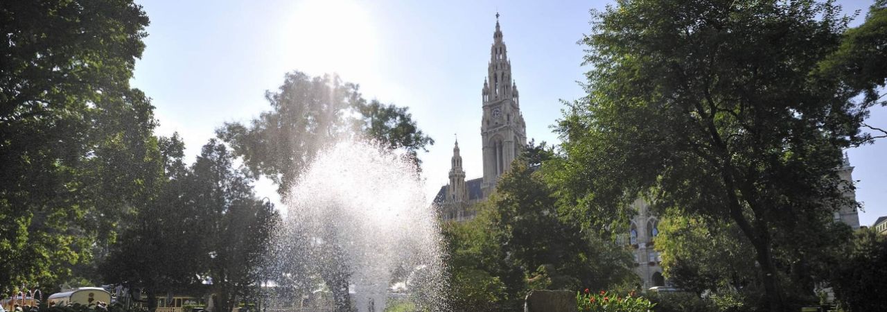 Das Wiener Rathaus vom Rathauspark aus gesehen. Im Vordergrund eine Wasserfontäne.