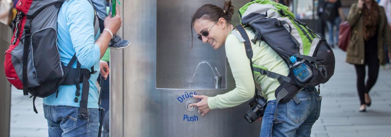 Eine Frau versorgt sich am Trinkbrunnen mit Wasser.