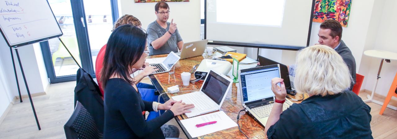 Mitarbeiter*innen mit Laptops an einem Besprechungstisch