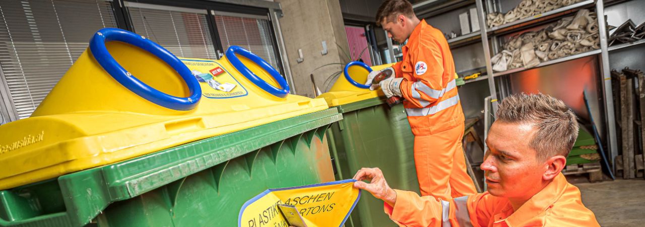 Mitarbeiter der MA 48 entfernen das Etikett von der gelben Tonne.