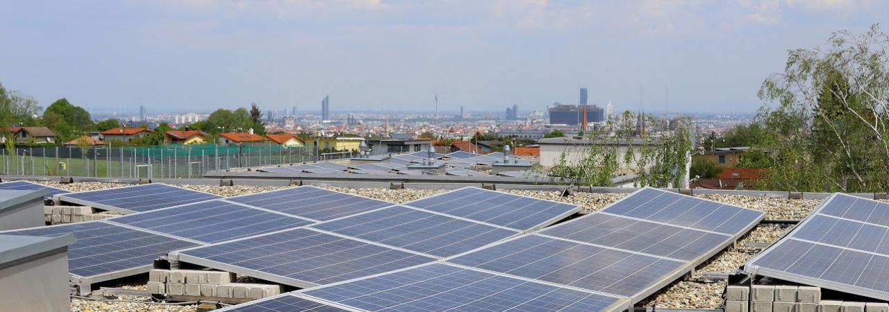 Photovoltaikanlage auf einem flachen Hausdach, im Hintergrund Blick auf Wien