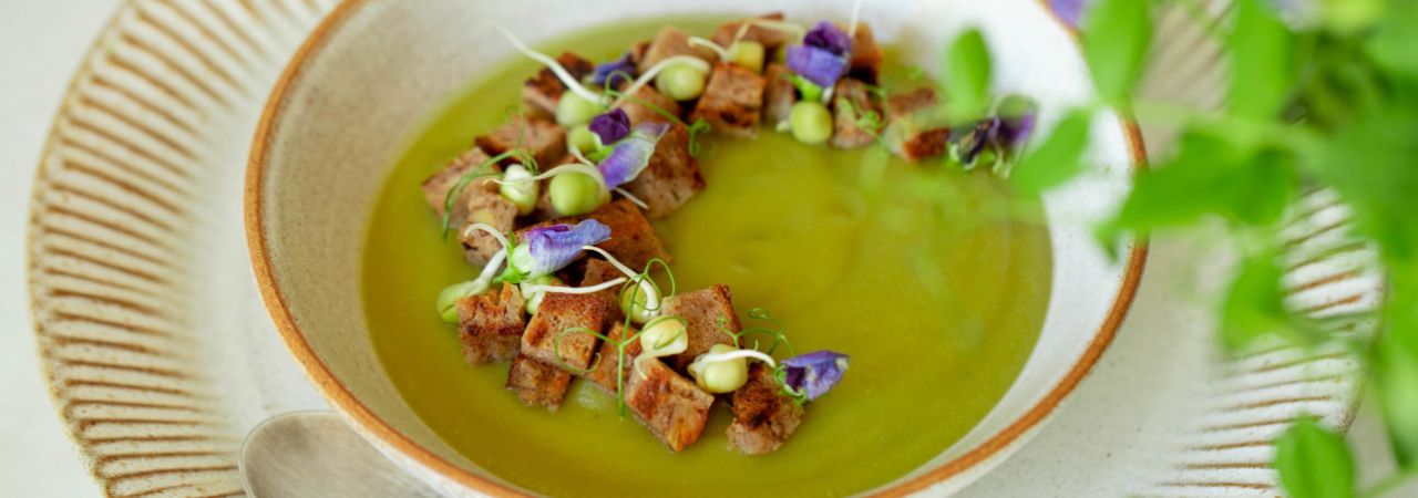 Ein Teller mit Erbsensuppe mit Croutons und Blüten