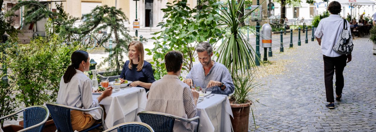 Vier Personen essen in einem Schanigarten.
