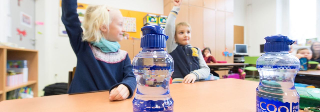 Két bécsi kisiskolás ül az iskolapadban, előttük vizespalack