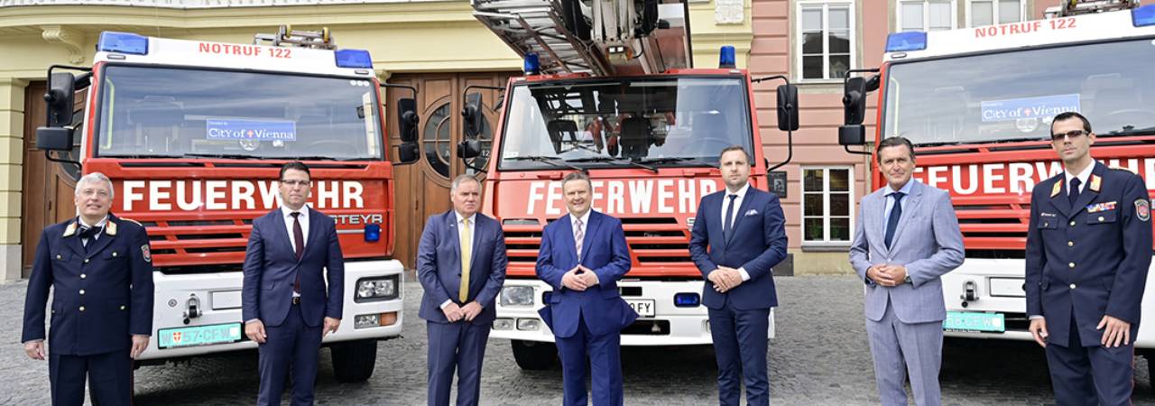 Bürgermeister Ludwig (Vierter von links) und Bürgermeister Skaka (rechts daneben) und weitere offizielle Vertreter vor drei Feuerwehrfahrzeugen