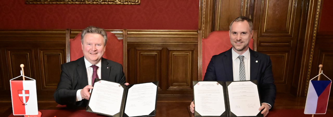 Bürgermeister Ludwig und Oberbürgermeister Hřib lächeln und halten die unterschriebenen Dokumente in die Kamera.