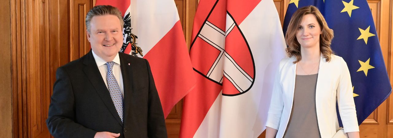 Wiens Bürgermeister Michael Ludwig und die  Primatorin von Brünn, Markéta Vaňková, stehen lächelnd vor drei Flaggen