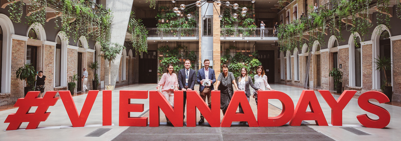 Organizers and representatives of the City of Vienna stand behind the waist-high styrofoam lettering #Viennadays in the leafy event location HubHub in Budapest