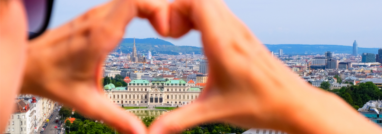 Two hands are forming a heart, through which one can see the panorama of the city of Vienna