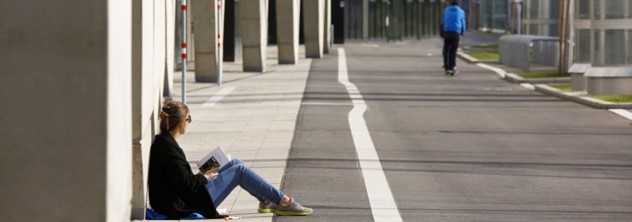 Fiatal lány ül a falnak támaszkodva a földön, azt utcán
