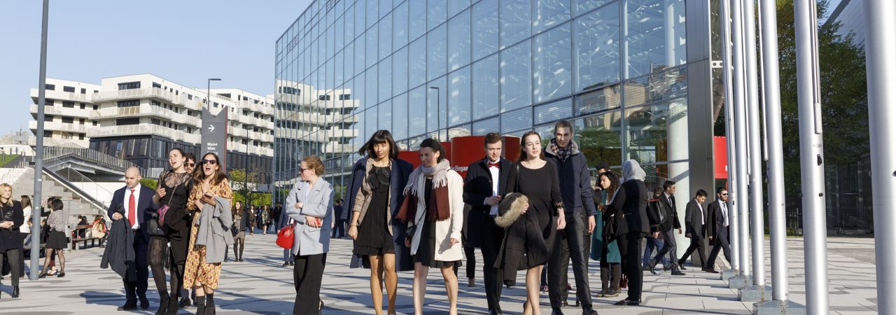 Menschen gehen auf der Straße, im Hintergrund ein modernes Gebäude