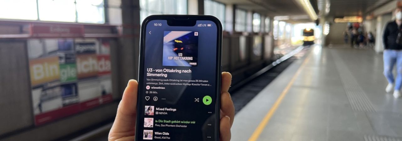 Mobilt tartó kéz, a kijelzőn az U3 playlistje a Spotify-on