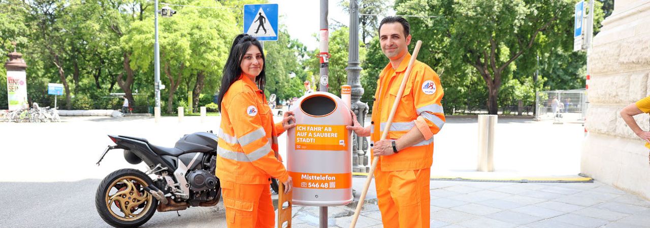 Zwei Mitarbeiter*innen der MA 48 stehen neben einem Mistkübel.
