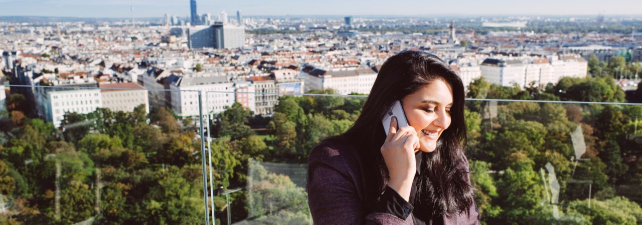 žena telefonira na balkonu s pogledom na grad