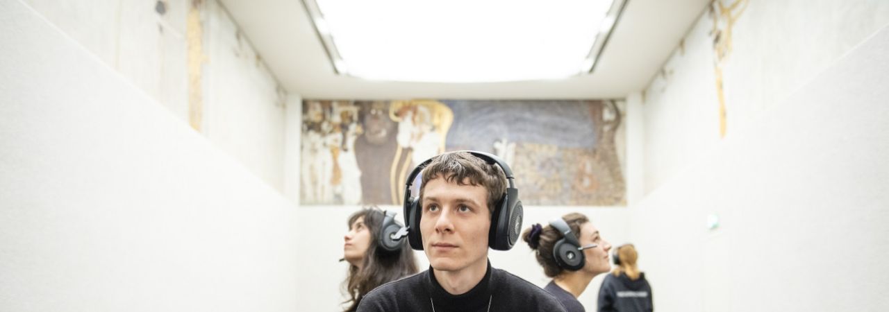 Fiatal férfi fülhallgatóval a fején Klimt Beethovenfríz című alkotása előtt