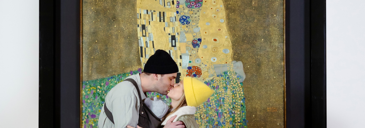 Млад мъж и жена се целуват пред картината на Климт