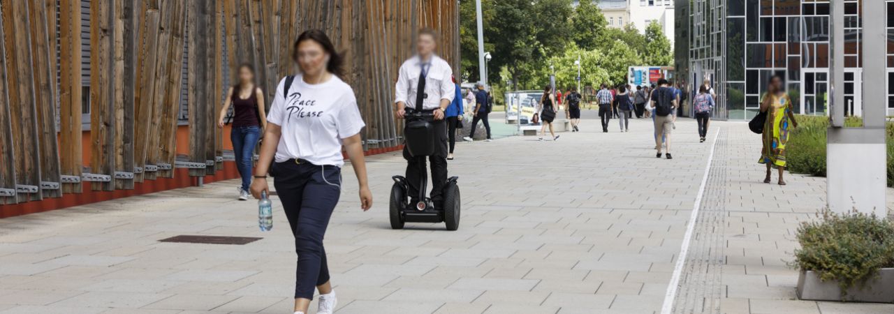Fußgänger*innen und Rollerfahrer*innen in einer Fußgängerzone