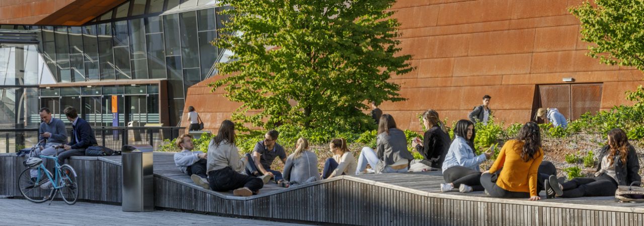 Junge Menschen sitzen auf Holzmobiliar im öffentlichen Raum