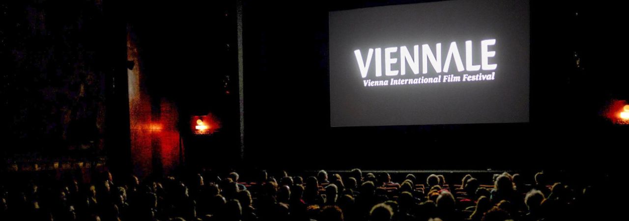 Gut besuchter Kinosaal mit Vienna-Schriftzug auf der Leinwand.
